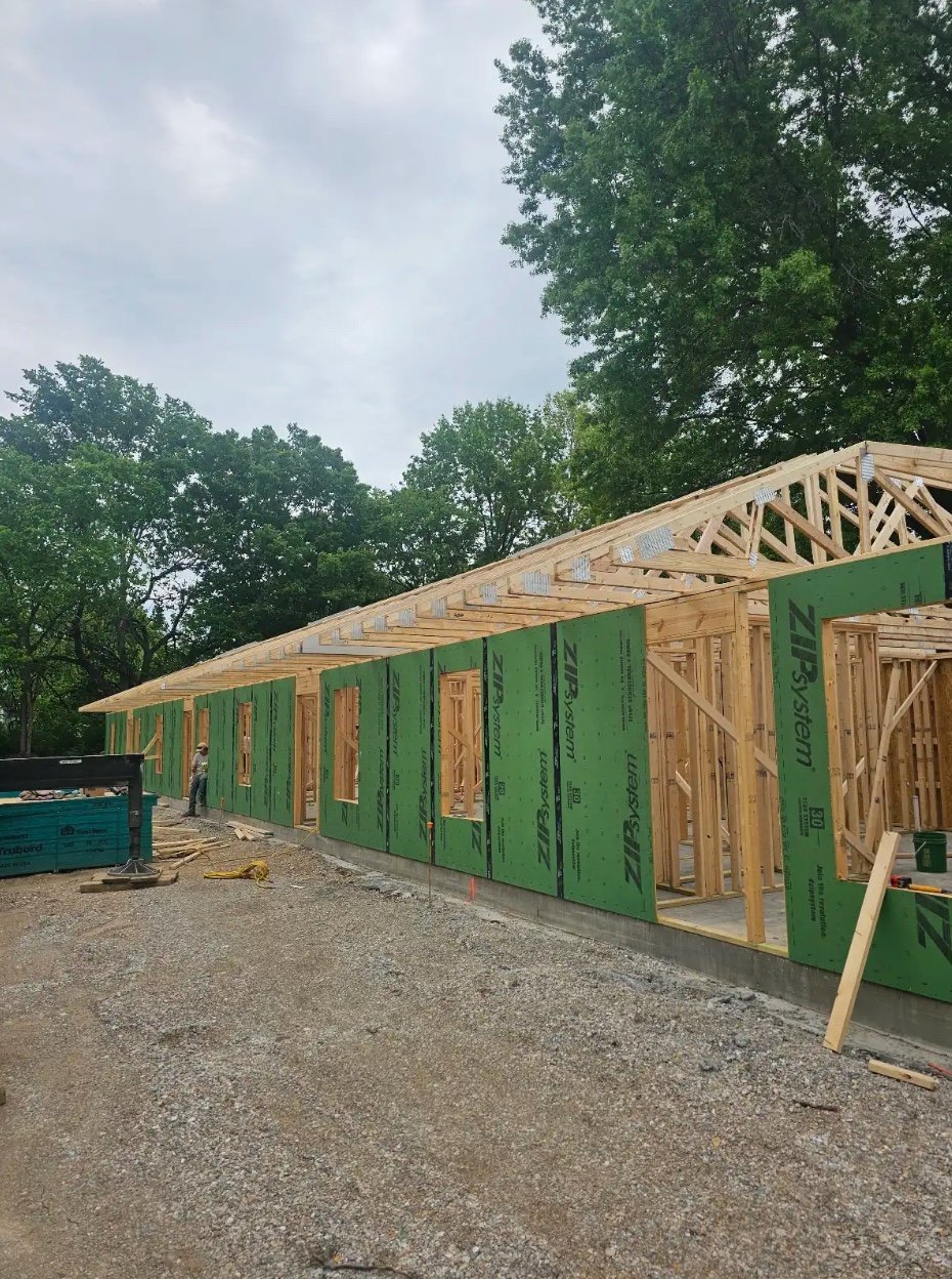Construction of a long green wooden building with exposed roof framing